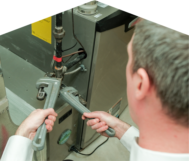 Francis plumbing specialist using two pipe wrenches to service a gas line connection beside a residential heating unit. Francis plumbing specialist using two pipe wrenches to service a gas line connection beside a residential heating unit.
