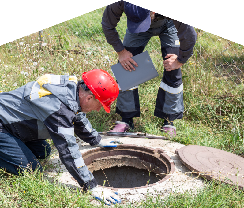 Francis sewer crew inspecting an open manhole in a grassy field, with one member documenting findings on a clipboard. Francis sewer crew inspecting an open manhole in a grassy field, with one member documenting findings on a clipboard.